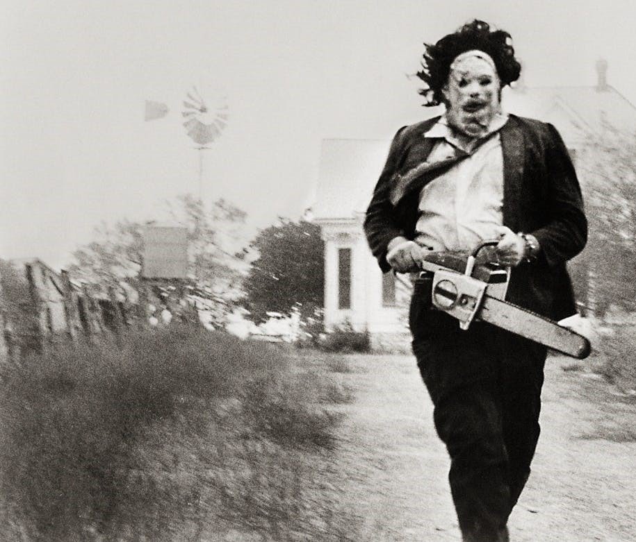 Black and white image of Leatherface from The Texas Chain Saw Massacre running from a house.