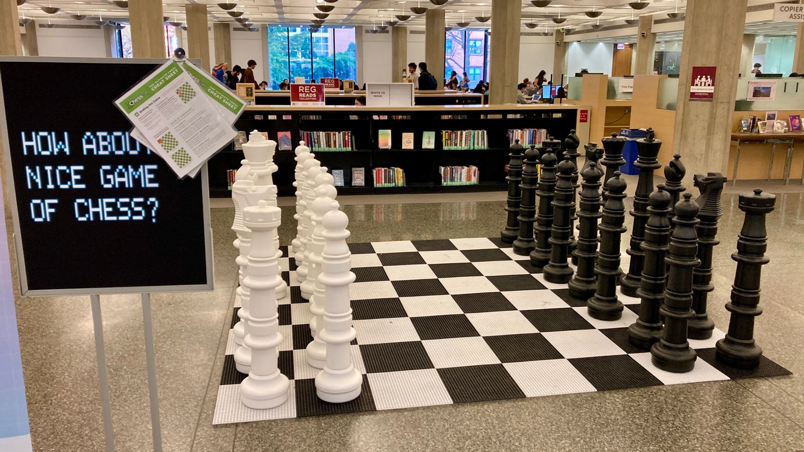 A large chess board nest to a sign that reads "How about a nice game of chess"